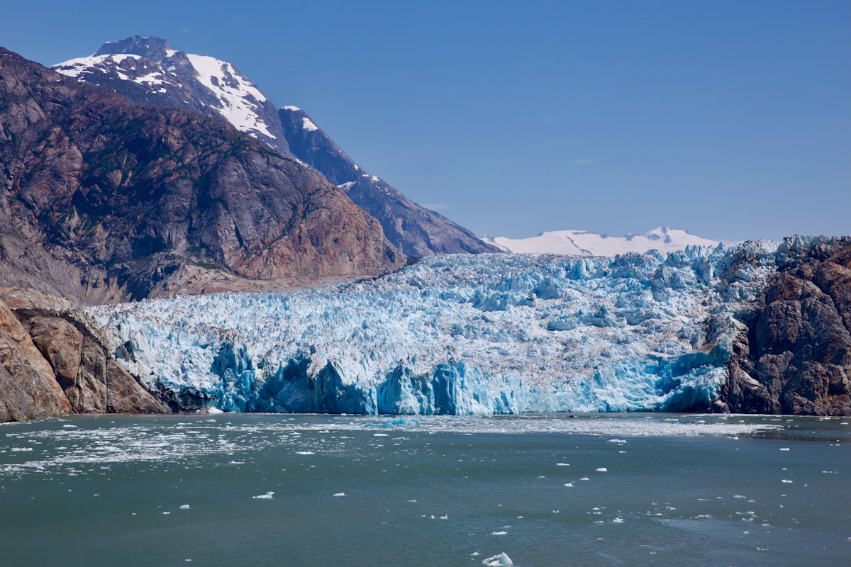 Blue glacier meeting the water beneath Alaska mountain peaks