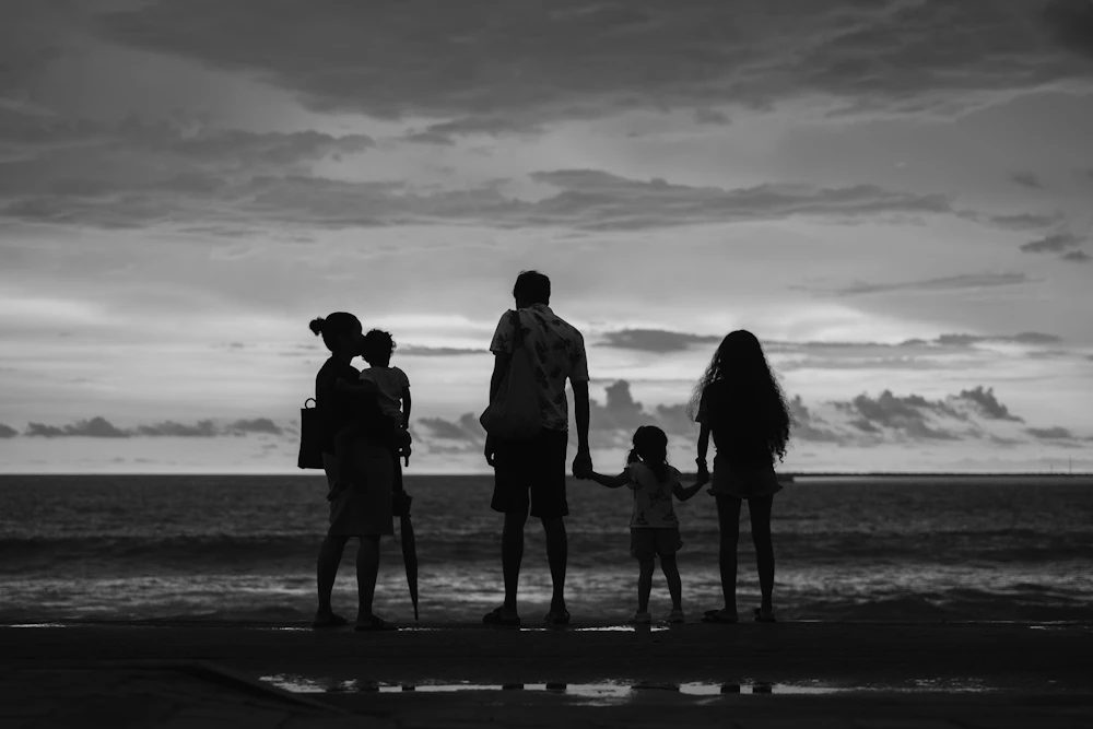 Family silhouettes sharing a quiet sunset beside the ocean