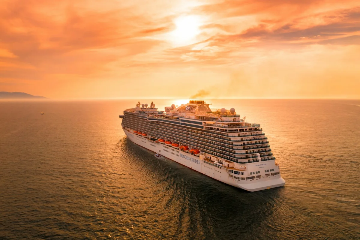 Ocean cruise ship sailing at sunset beneath a colorful sky