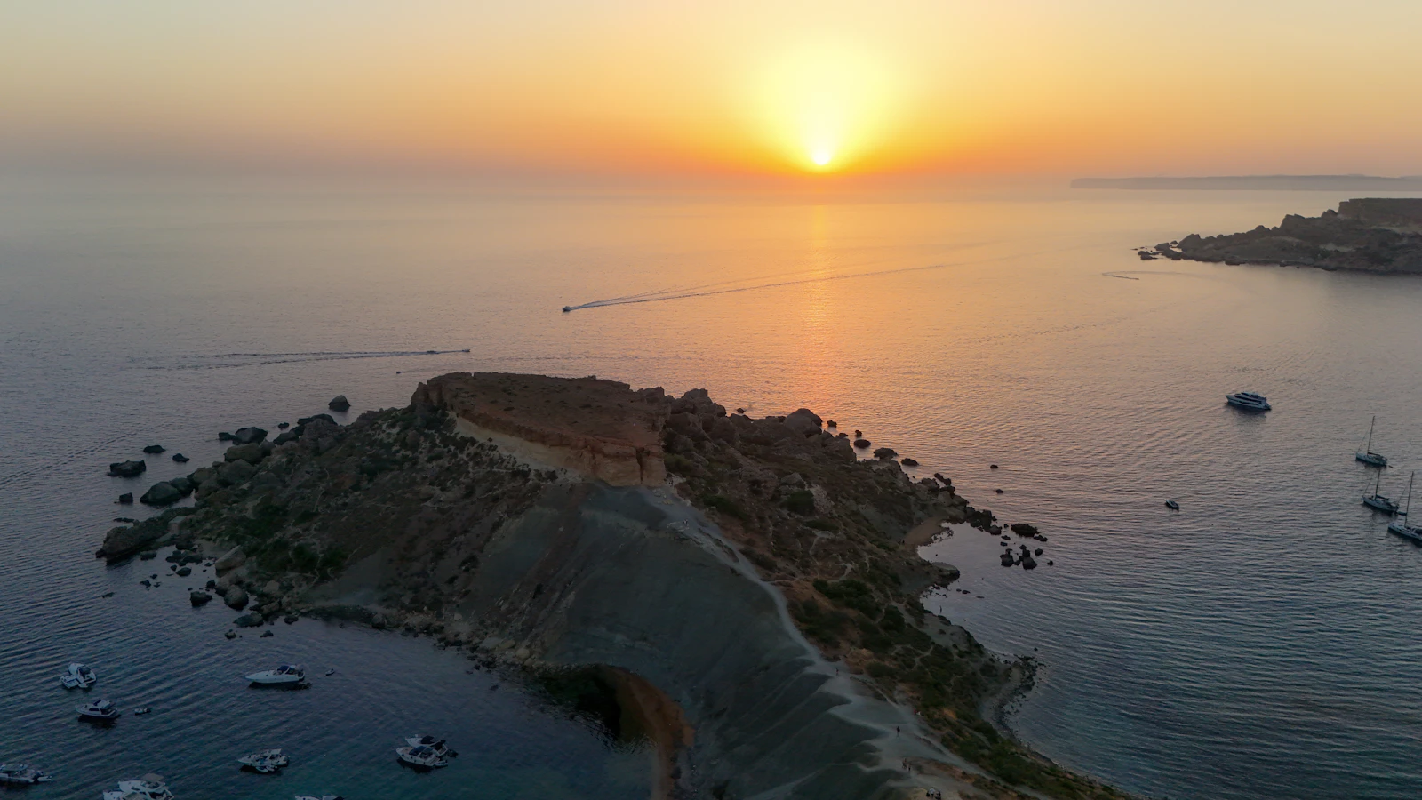 Small boats surrounding a Mediterranean island at sunset